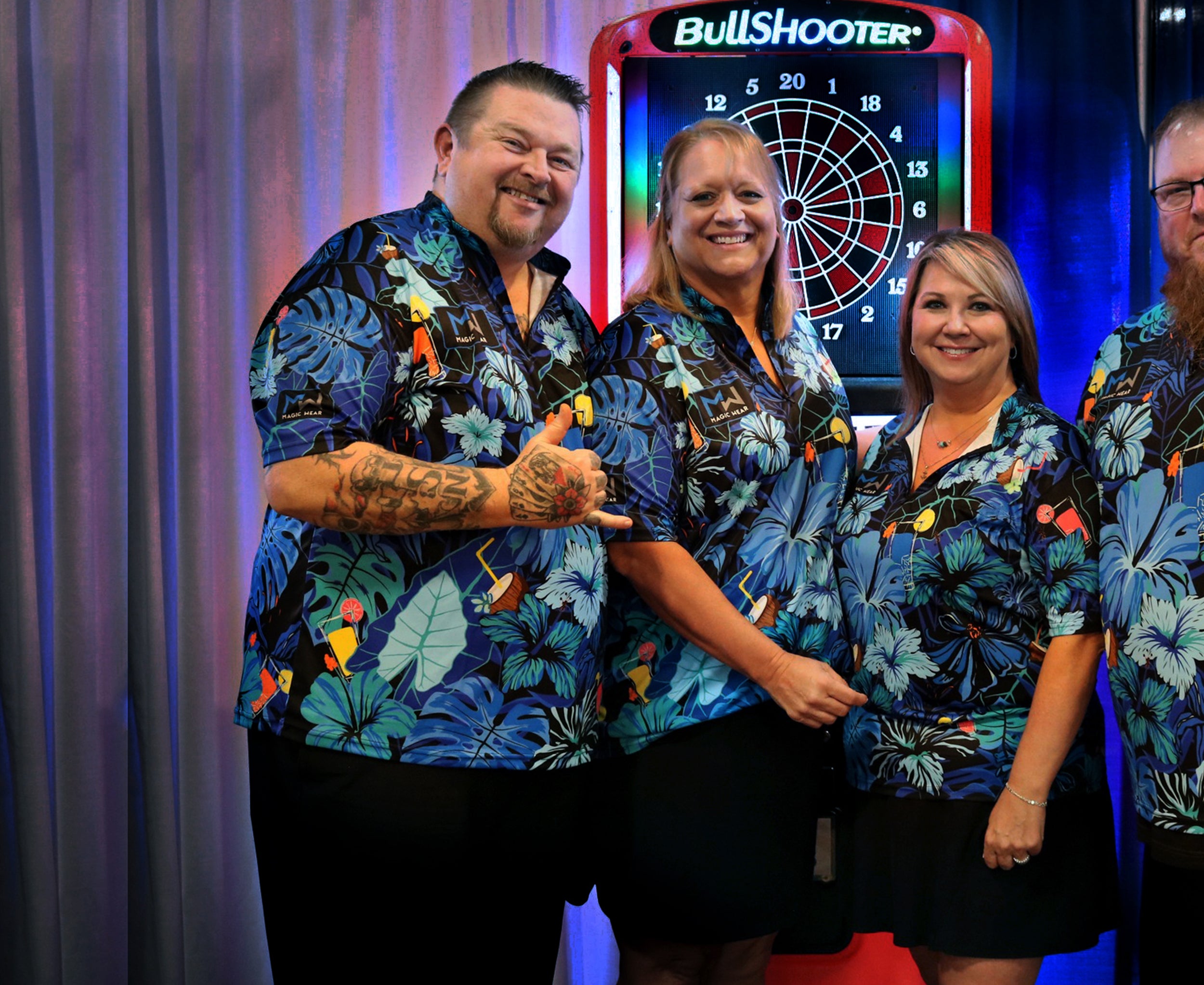 Four people in matching Hawaii Pau Hana floral jerseys standing in front of a Bullshooter dartboard.