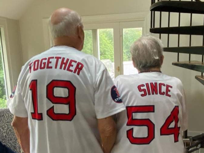 Two people wearing matching baseball jerseys with numbers and text, standing together.